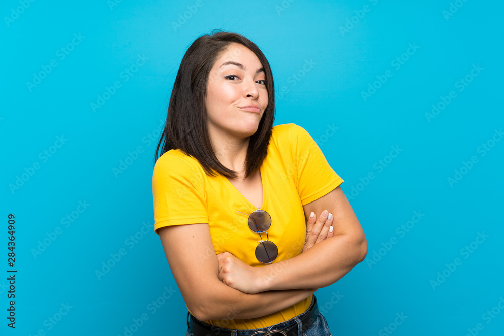 Young Mexican woman over isolated blue background making doubts gesture while lifting the shoulders Young Mexican woman over isolated blue background making doubts gesture while lifting the shoulders