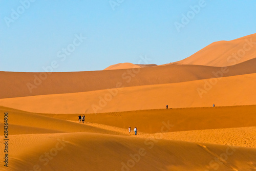 Tourists hiking on red sand dune in southern Namib Desert, Sossusvlei, Namib-Naukluft National Park. Hardap Region, Namibia.