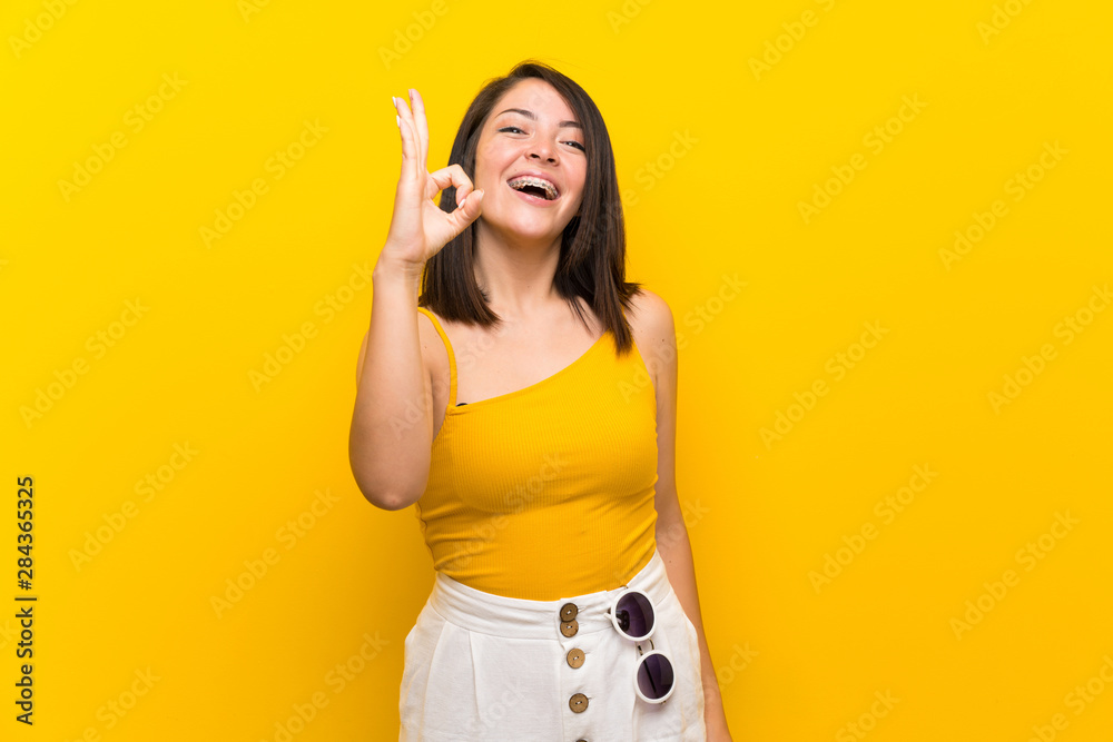 Young Mexican woman over isolated yellow background showing ok sign with fingers Young Mexican woman over isolated yellow background showing ok sign with fingers