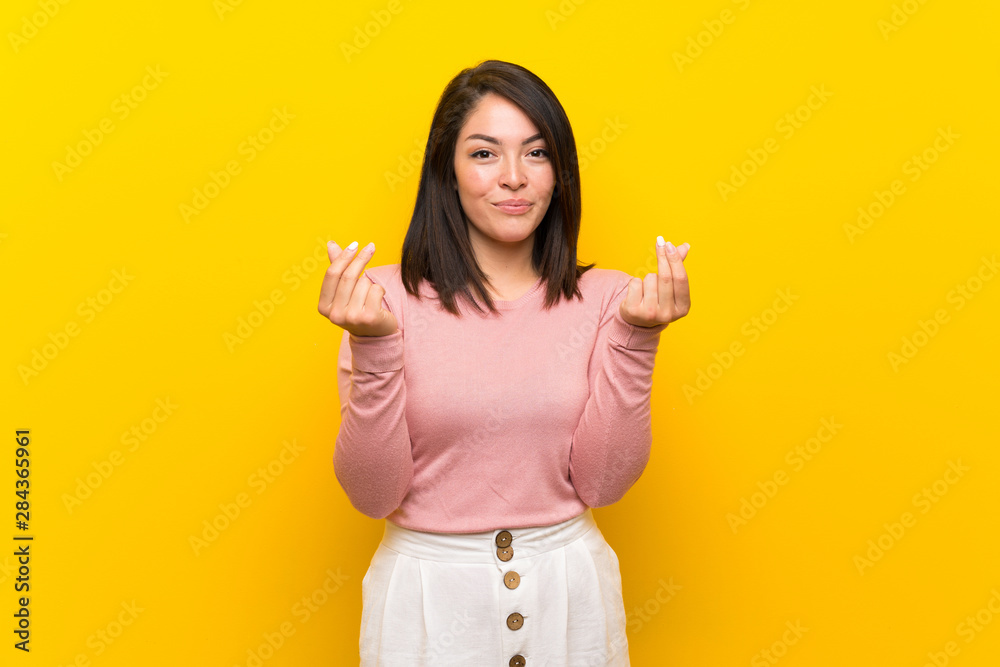 Young Mexican woman over isolated yellow background making money gesture Young Mexican woman over isolated yellow background making money gesture
