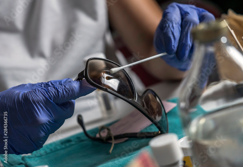 Police specialist examines pin of glasses stained with blood belonging to the victim of murder, conceptual image