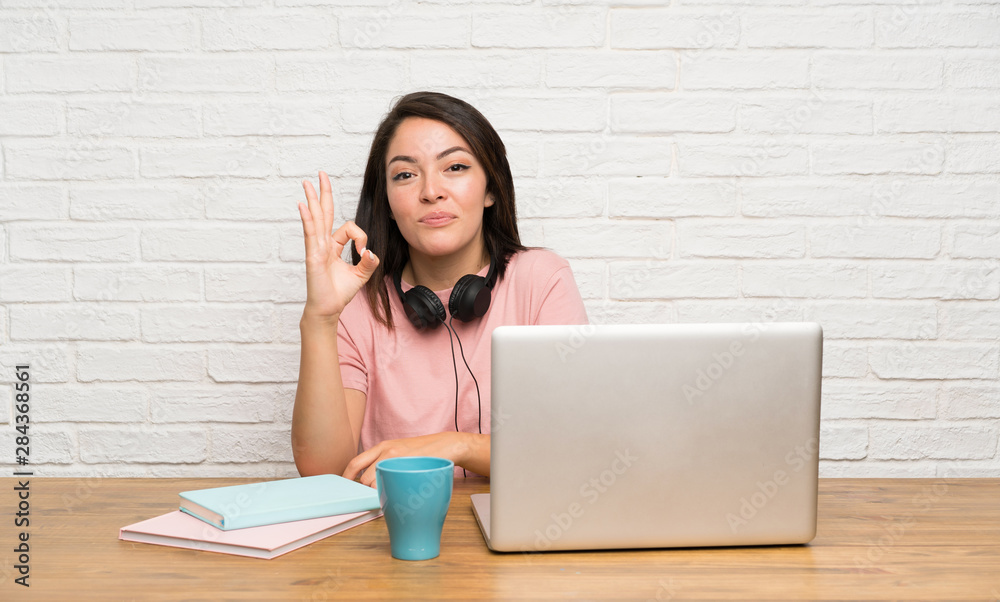 Young Mexican woman with a laptop showing an ok sign with fingers Young Mexican woman with a laptop showing an ok sign with fingers