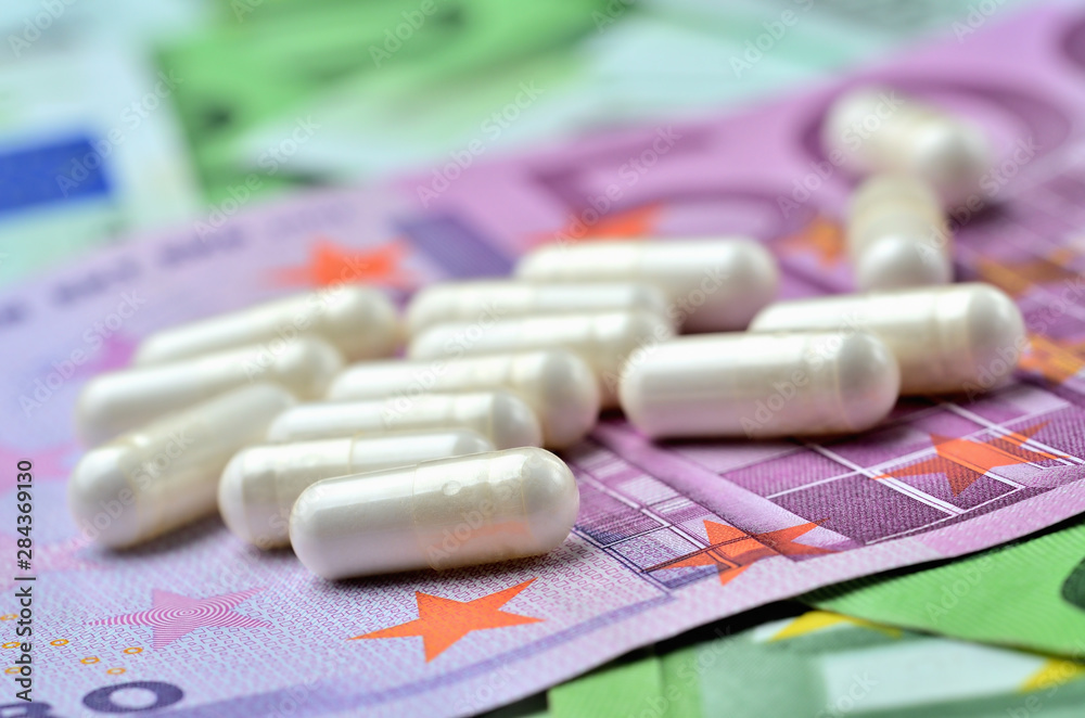 Close-up of white capsule pills on euro banknotes - concept of healthcare and finance Close-up of white capsule pills on euro banknotes - concept of healthcare and finance