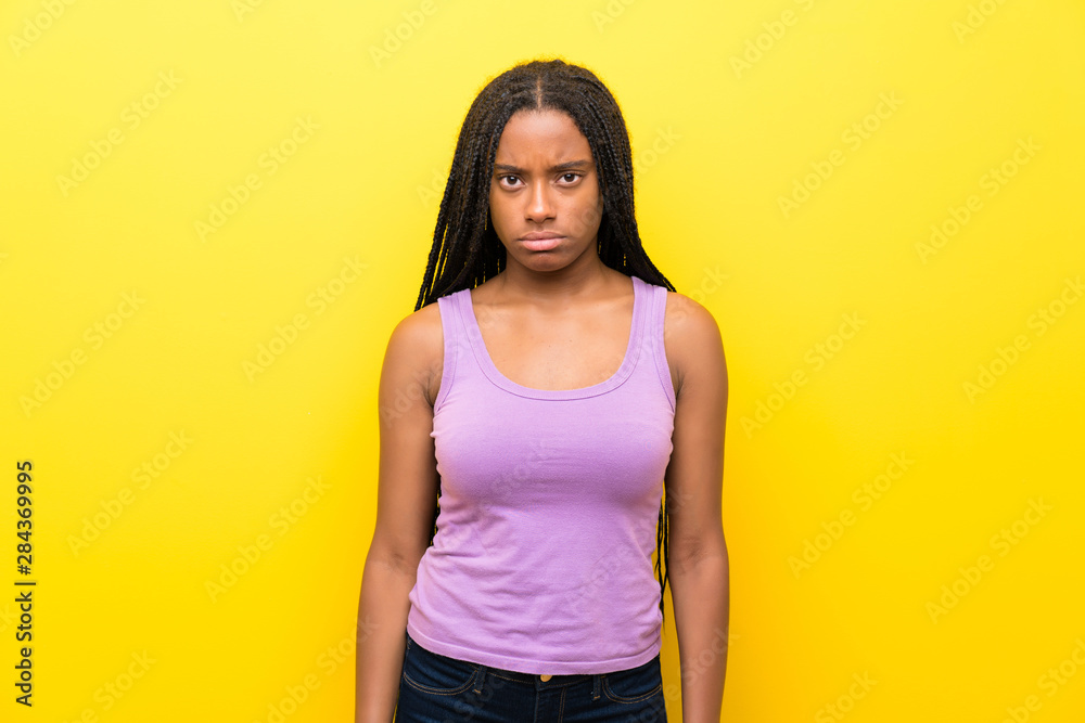 African American teenager girl with long braided hair over isolated yellow wall with sad and depressed expression African American teenager girl with long braided hair over isolated yellow wall with sad and depressed expression