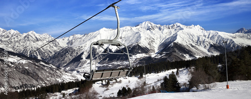Ski slope and chair-lift in snow winter mountains at sun windy day