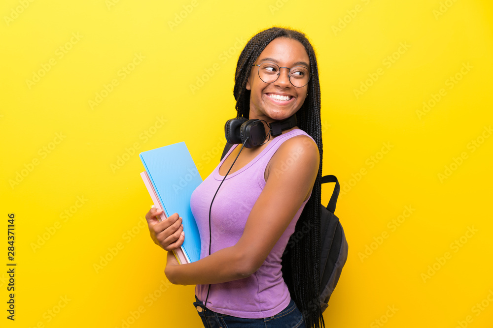 African American teenager student girl with long braided hair over isolated yellow wall laughing African American teenager student girl with long braided hair over isolated yellow wall laughing
