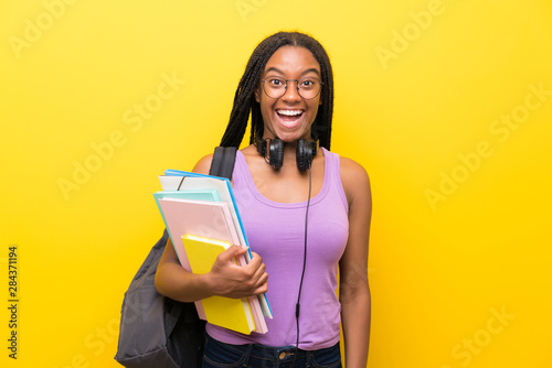 African American teenager student girl with long braided hair over isolated yellow wall with surprise facial expression