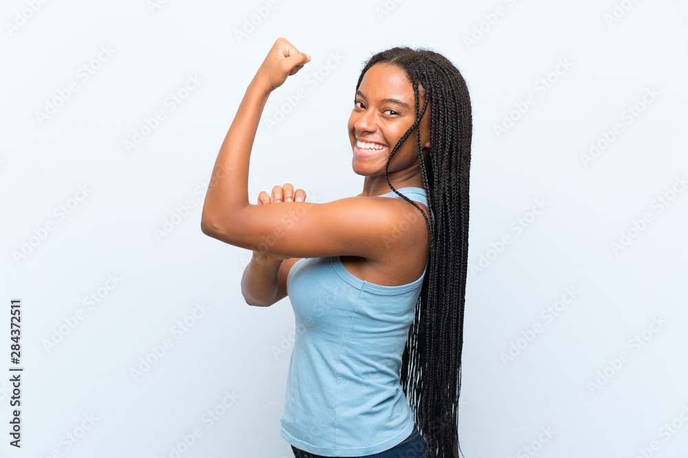 African American teenager girl with long braided hair over isolated blue background making strong gesture African American teenager girl with long braided hair over isolated blue background making strong gesture