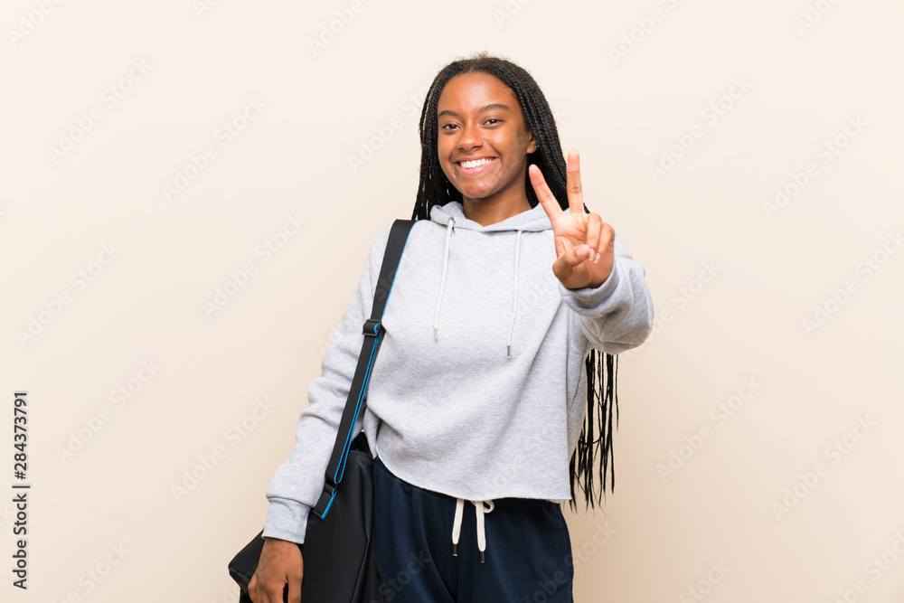 African American sport teenager girl with long braided hair smiling and showing victory sign