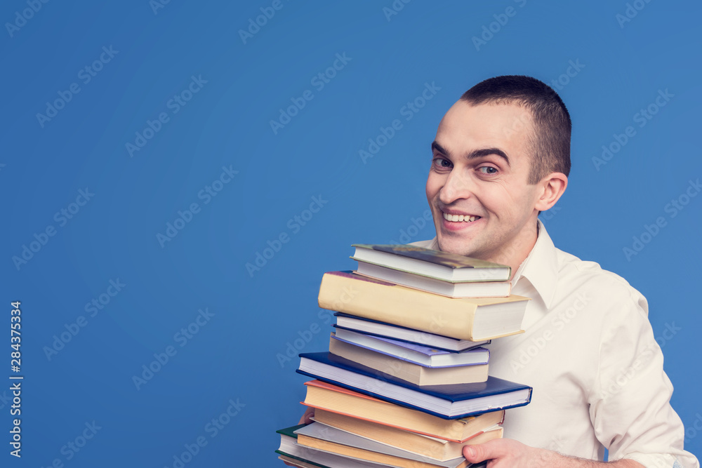 Portrait, student in the white shirt with books, looking at the camera, blue background, front view, copy space, the concept of heavy loads in education Portrait, student in the white shirt with books, looking at the camera, blue background, front view, copy space, the concept of heavy loads in education