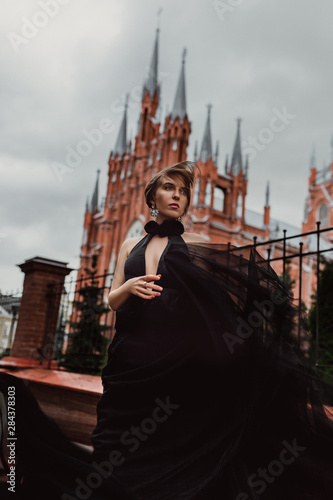 Gothic image. Beautiful girl in a black magnificent dress on a background of the castle. Spectacular woman travels around the country. Gothic castle. Girl in an elegant evening dress. photo