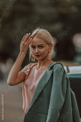 Street portrait of a stylish girl. Cute blonde on the street. Beautiful woman in a jacket stands on the street. Stylish accessories on a girl
