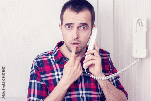 Handsome man talking on the intercom or phone land line, male in confusion, portrait, close up, toned photo