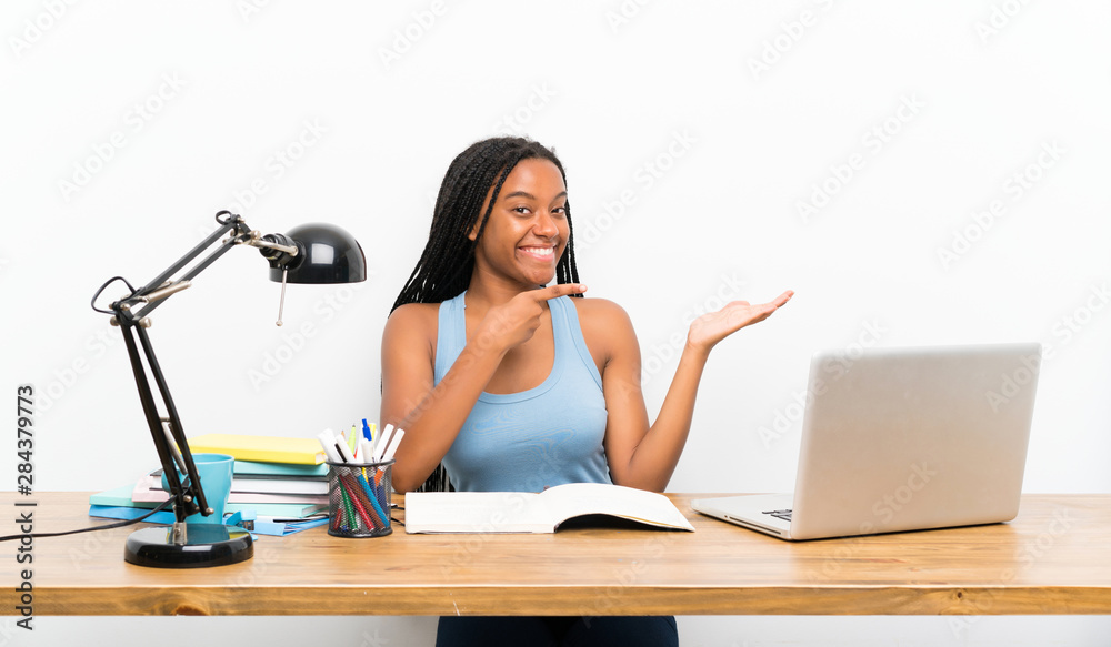 African American teenager student girl with long braided hair in her workplace holding copyspace imaginary on the palm to insert an ad African American teenager student girl with long braided hair in her workplace holding copyspace imaginary on the palm to insert an ad
