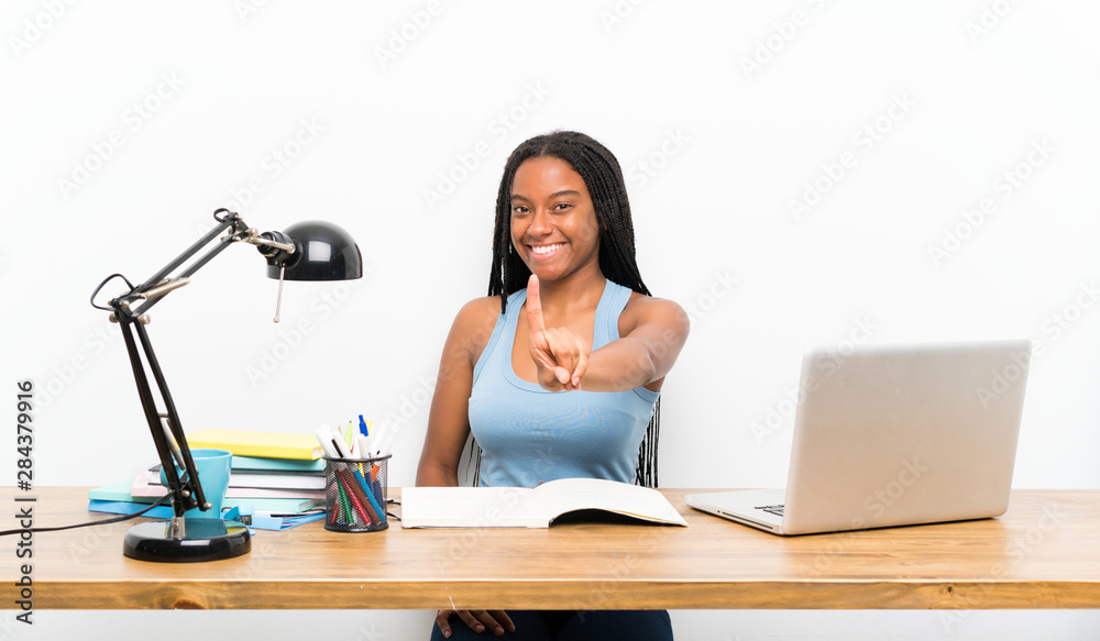 African American teenager student girl with long braided hair in her workplace showing and lifting a finger African American teenager student girl with long braided hair in her workplace showing and lifting a finger