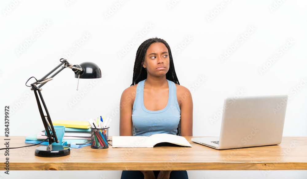 African American teenager student girl with long braided hair in her workplace making doubts gesture looking side African American teenager student girl with long braided hair in her workplace making doubts gesture looking side