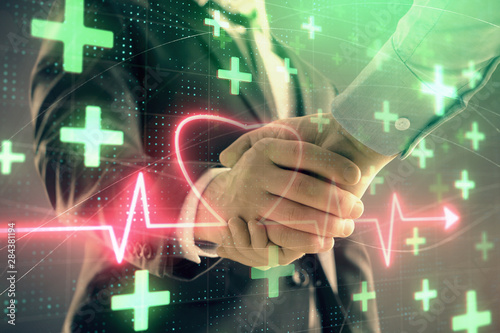 Multi exposure of heart hologram on abstract background with two men handshake. Concept of medical education