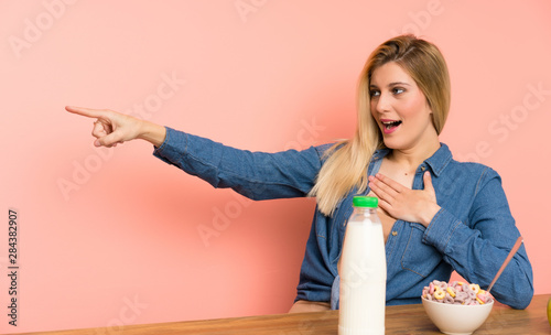 Young blonde woman with bowl of cereals pointing finger to the side