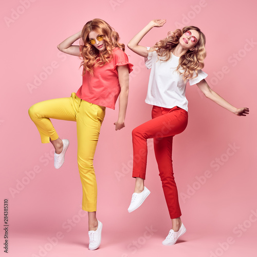 Two easy-going happy hipster Woman dance Fun in Stylish fashion colored red yellow pants. Beautiful excited Girl in summer Trendy outfit, sneakers jump laughing. Creative dancing fashionable concept