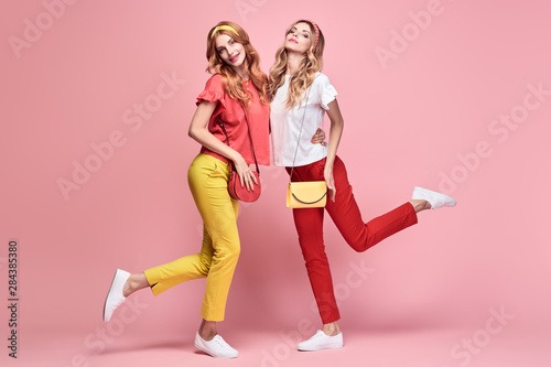 Fashionable embracing woman smiling on pink background. Two Shapely Girl sisters Having Fun dance, Trendy yellow coral summer outfit, fashion hairstyle, makeup. Gorgeous female model, funny concept