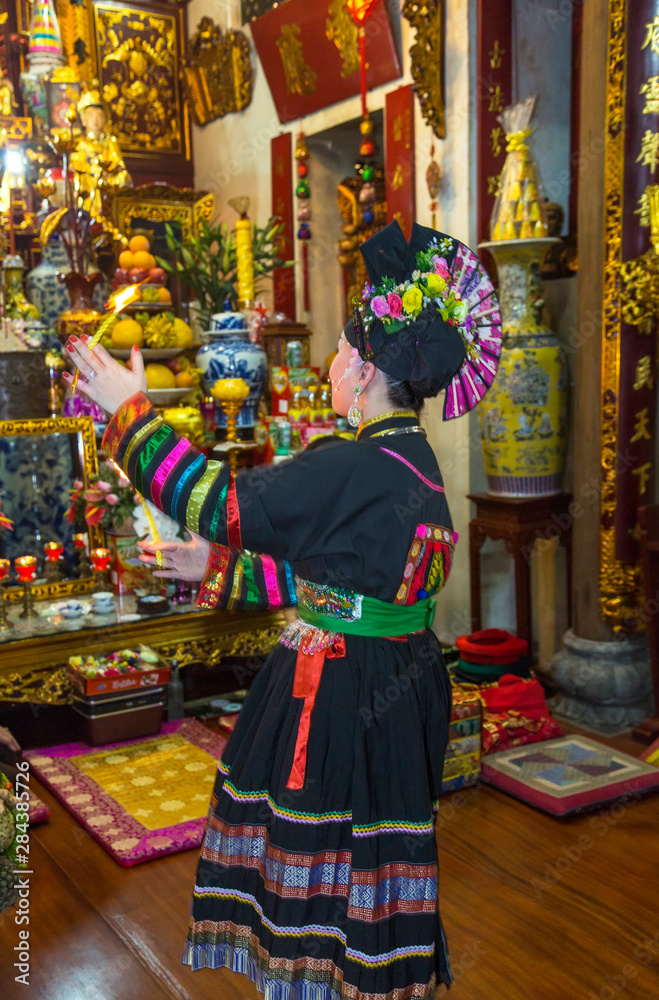 Woman in traditional dress performing ceremony in temple, Hanoi, Vietnam