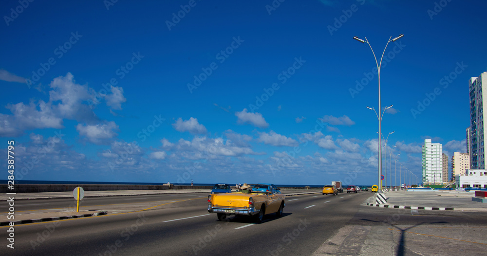 Havana, Cuba, colorful cars along the Malecon Highway and the water with some buildings in the background