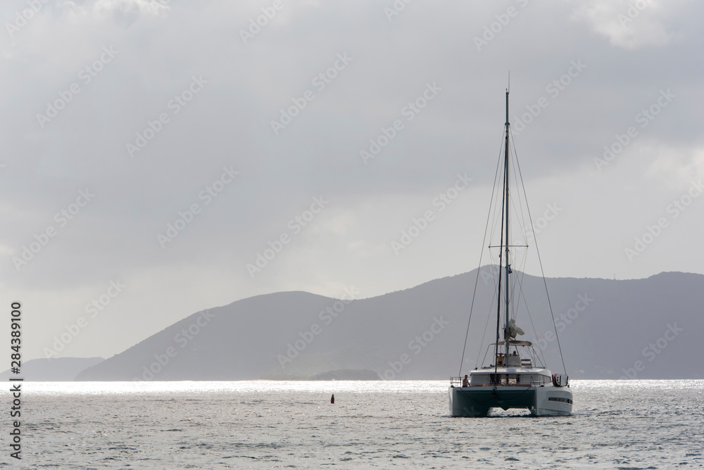 UK, British Virgin Islands, Catamaran navigates gray sky reflected calm Caribbean Sea
