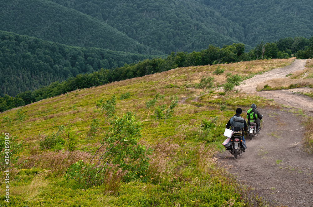 Mountain landscape. Blueberry pickers in the mountains of the Carpathians, covered with green bilberry, on motorbikes ride on a country road. People and their traditions. Photo from the back. Mountain landscape. Blueberry pickers in the mountains of the Carpathians, covered with green bilberry, on motorbikes ride on a country road. People and their traditions. Photo from the back.