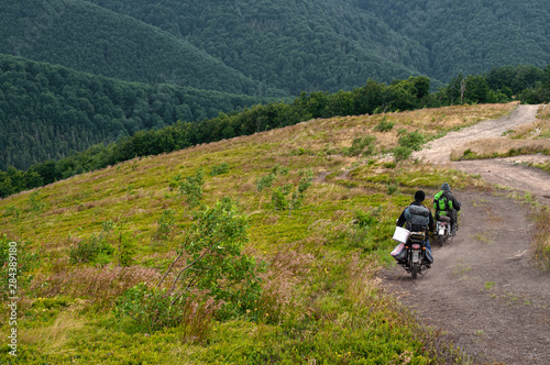 Mountain landscape. Blueberry pickers in the mountains of the Carpathians, covered with green bilberry, on motorbikes ride on a country road. People and their traditions. Photo from the back.
