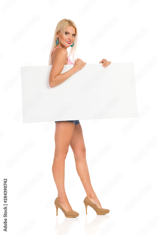 Beautiful Blond Woman Standing With White Poster Under Her Arm. Side View. Beautiful Blond Woman Standing With White Poster Under Her Arm. Side View.
