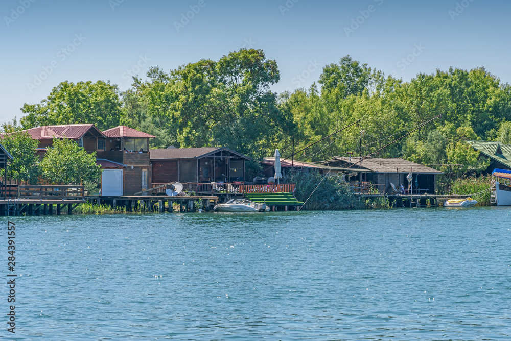 River Bojana and small wooden houses with marinas and boats on the riverbank for tourists. Water landscape