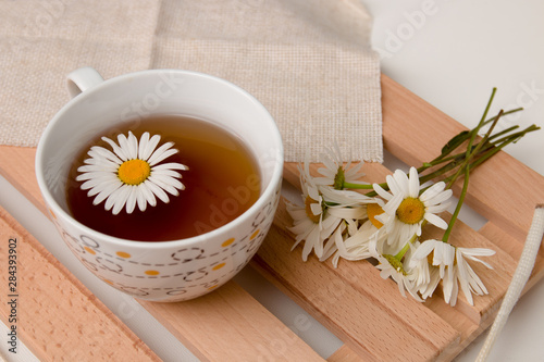 cup with chamomile tea on a beige fabric with daisies on a wooden tray white background isolation top view copy space