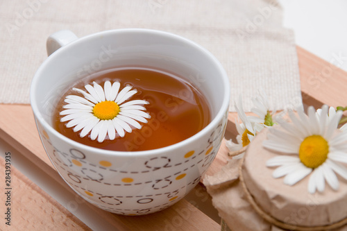 cup with chamomile tea on a beige fabric with daisies on a wooden tray white background isolation top view copy space