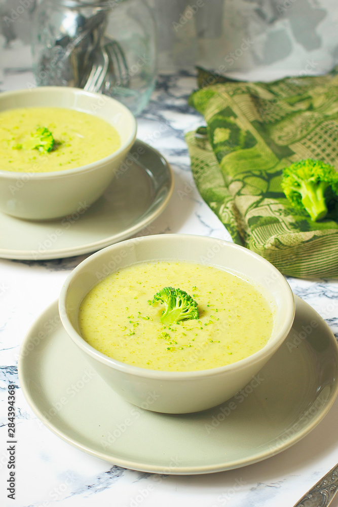 Fresh Broccoli cream soup on two gray ceramic bowl on plate with spoon on marble background,vegetarian food,healthy concept Fresh Broccoli cream soup on two gray ceramic bowl on plate with spoon on marble background,vegetarian food,healthy concept