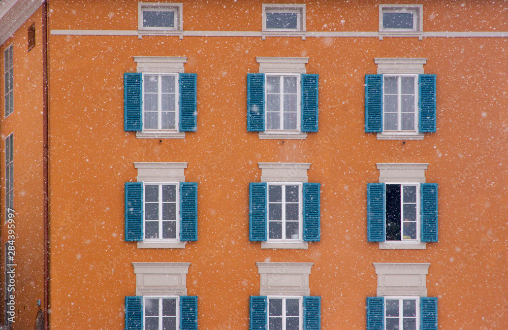 Austria, Salzburg. Blue shutters on orange apartment building in snowfall. (UNESCO World Heritage Site)