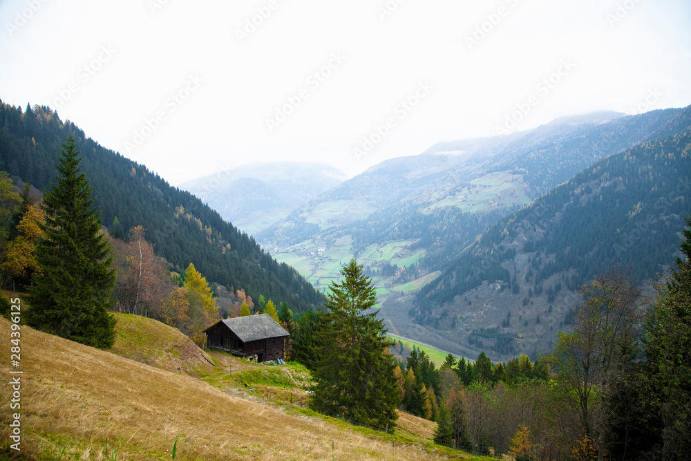 Austria - View of a picturesque, green mountains and a valley. A rustic building is viewable on the hillside.