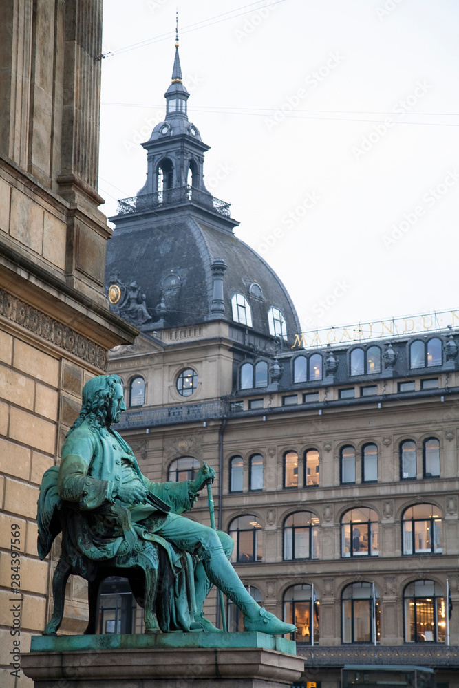 Copenhagen, Denmark - A statue of a man sitting in a chair wearing 18th century clothes is outside a building.
