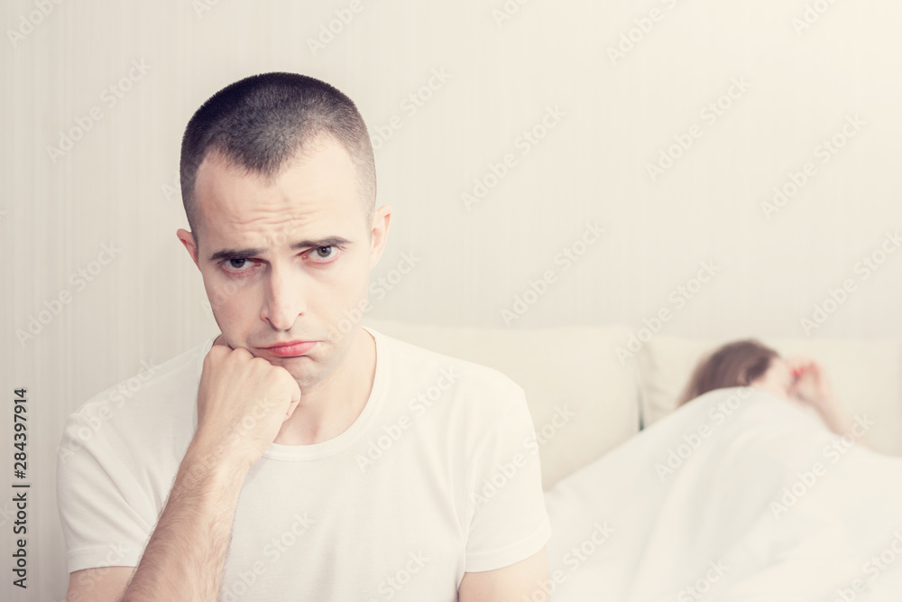 A attractive man and a woman in the bedroom, a girlfriend in the background, a sad man sitting on the bed, toned, the concept of problems in sex A attractive man and a woman in the bedroom, a girlfriend in the background, a sad man sitting on the bed, toned, the concept of problems in sex