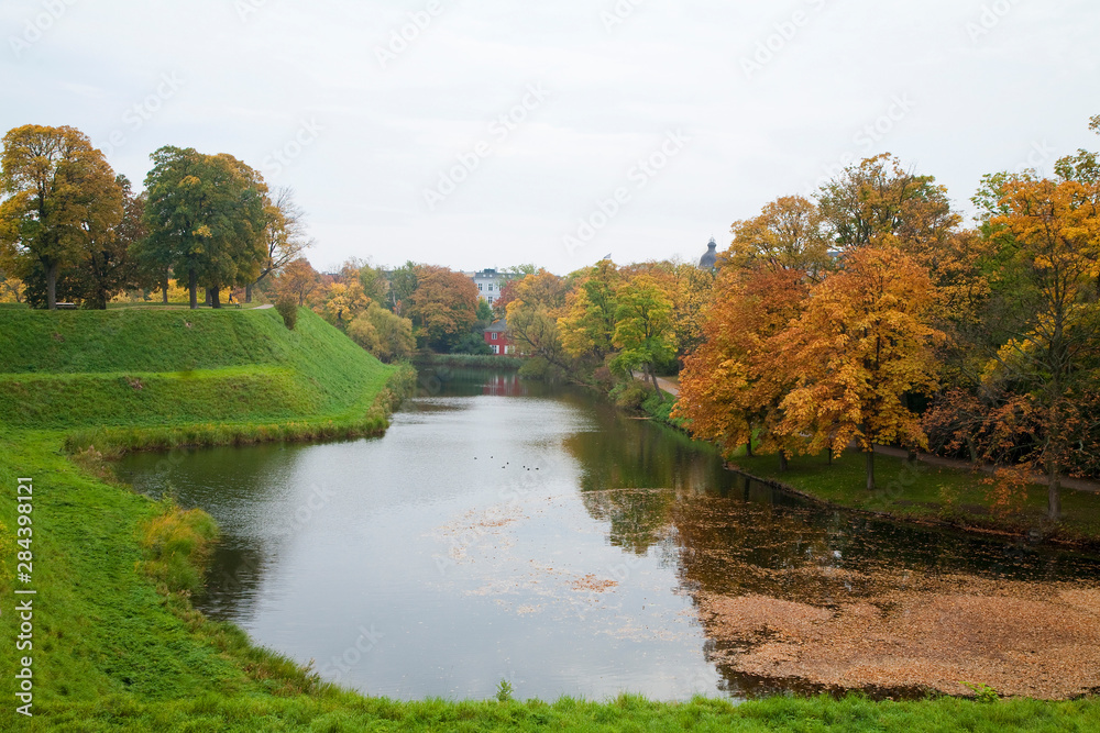 Fototapeta premium Copenhagen, Denmark - A river flows through the countryside. The reflection of trees on one side can be seen.
