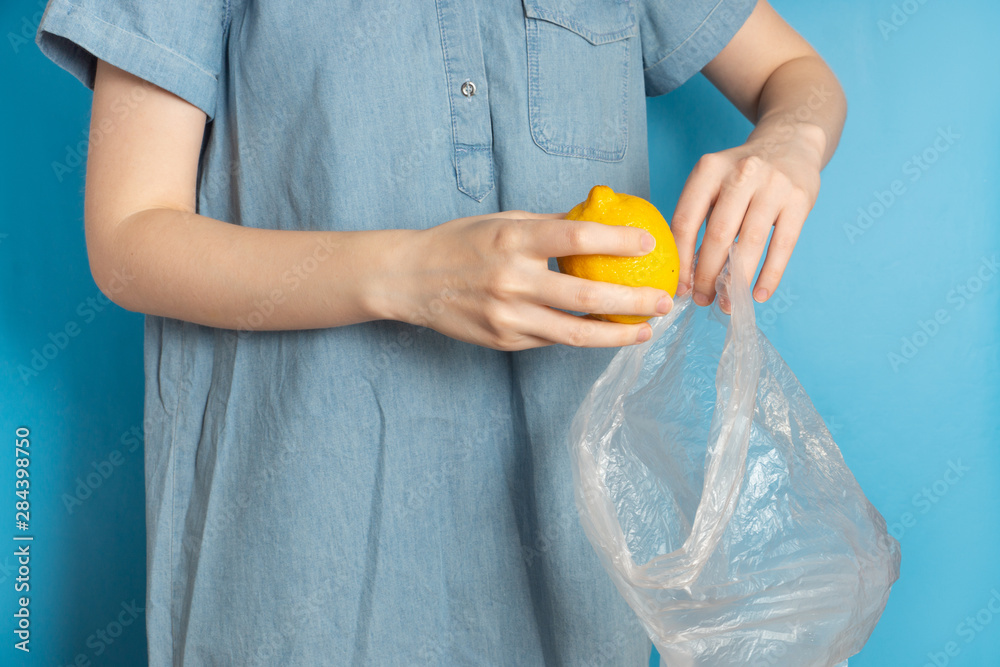 Woman puts lemon in plastic bag on blue background Woman puts lemon in plastic bag on blue background