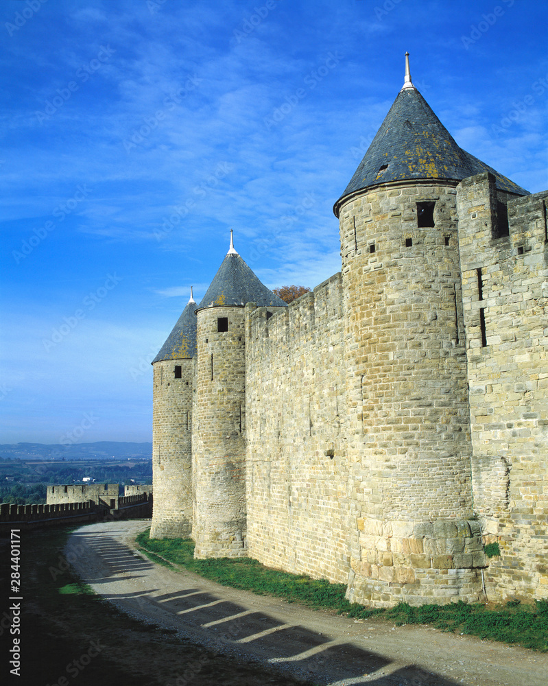 France, Carcassonne. Shadows of the crenelatted walls shade the pathway under the towers at La Cite in Carcassonne, Dept. Aude, France.