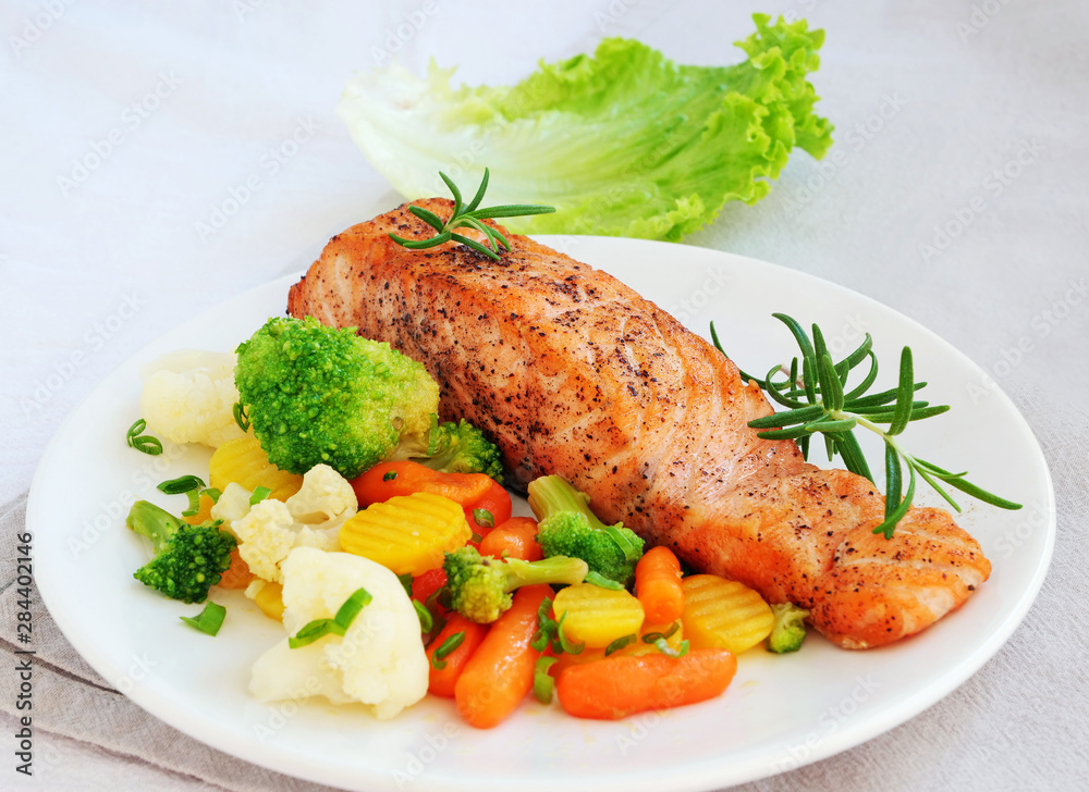 Grilled salmon fillet with vegetables lemon and rosemary over white plate Grilled salmon fillet with vegetables lemon and rosemary over white plate