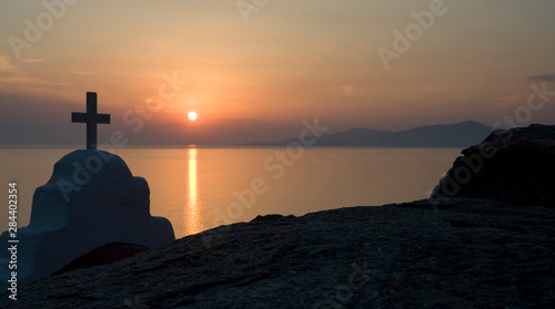 Greece, Mykonos, Hora. Sunset silhouettes Greek Orthodox church and cross in foreground.
