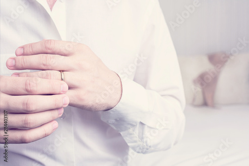 Unfaithful husband puts on a wedding ring on his finger, sitting on the bed in the hotel, women's underwear in the background, closeup, cropped image, toned. The concept of infidelity in marriage