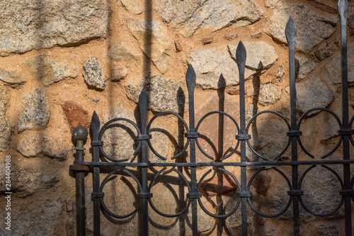 Italy, Sardinia, Gavoi. An iron gate casting a shadow on a rough stone wall.
