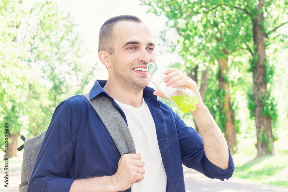 Joyful traveler with backpack drinks juice, man quenches his thirst, portrait, close up, toned Joyful traveler with backpack drinks juice, man quenches his thirst, portrait, close up, toned
