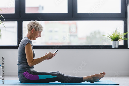 Senior woman using smartphone at home after exercise. The use of technology by the elderly.