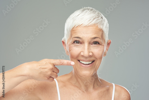 Beautiful Caucasian  smiling senior woman with short grey hair pointing at her teeth and looking at camera. Beauty photography. photo