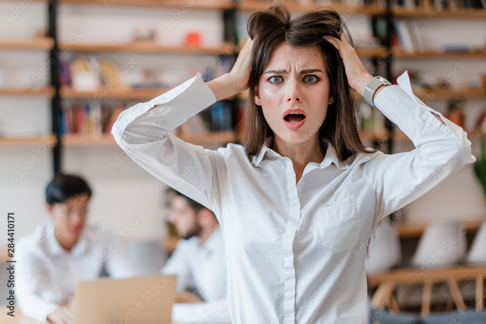 stressed out woman in the office holding her head shocked