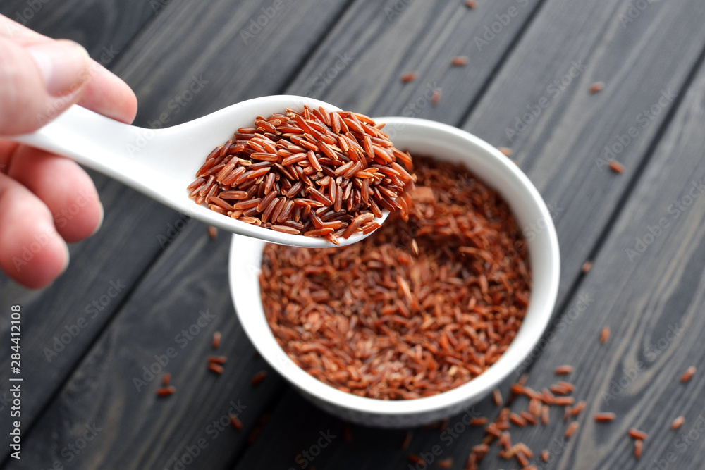 hand holdind a spoon with uncooked red rice hand holdind a spoon with uncooked red rice
